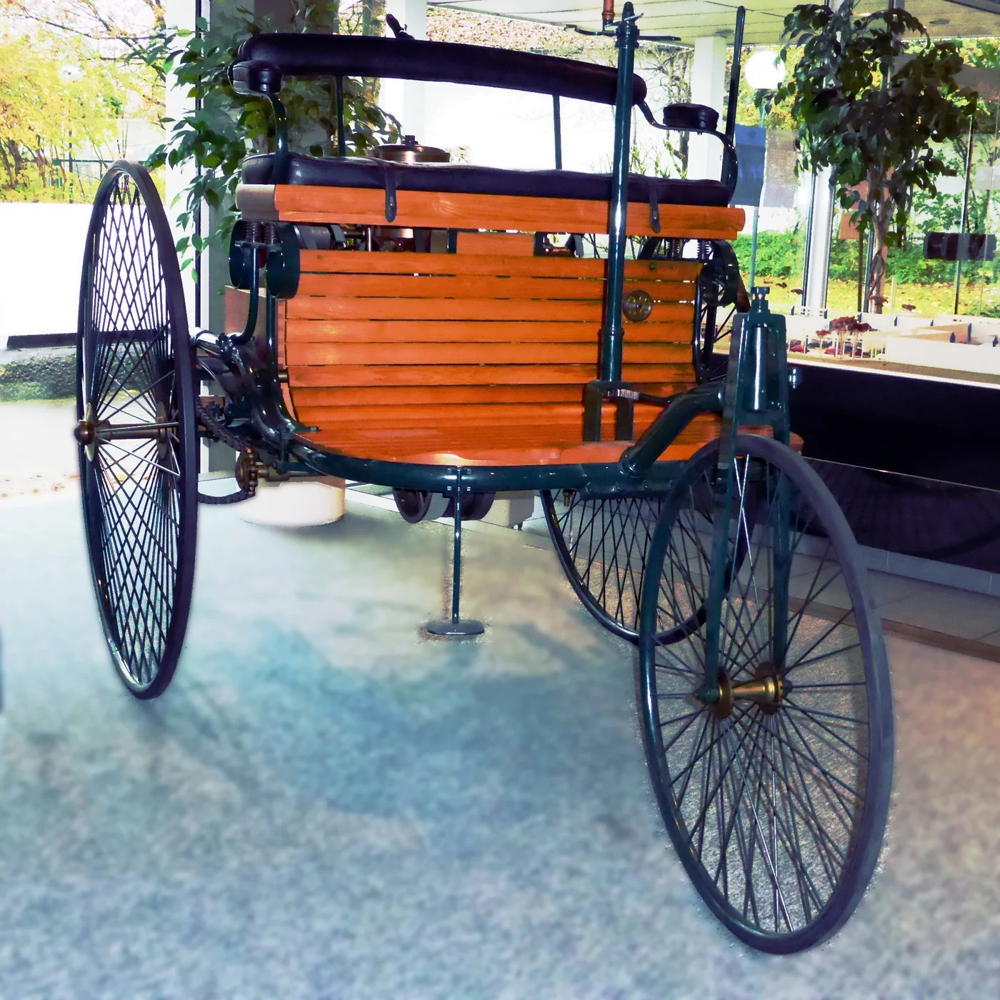 A preserved 1886 Benz Patent-Motorwagen with three wire-spoked wheels, an exposed engine, and a black bench seat